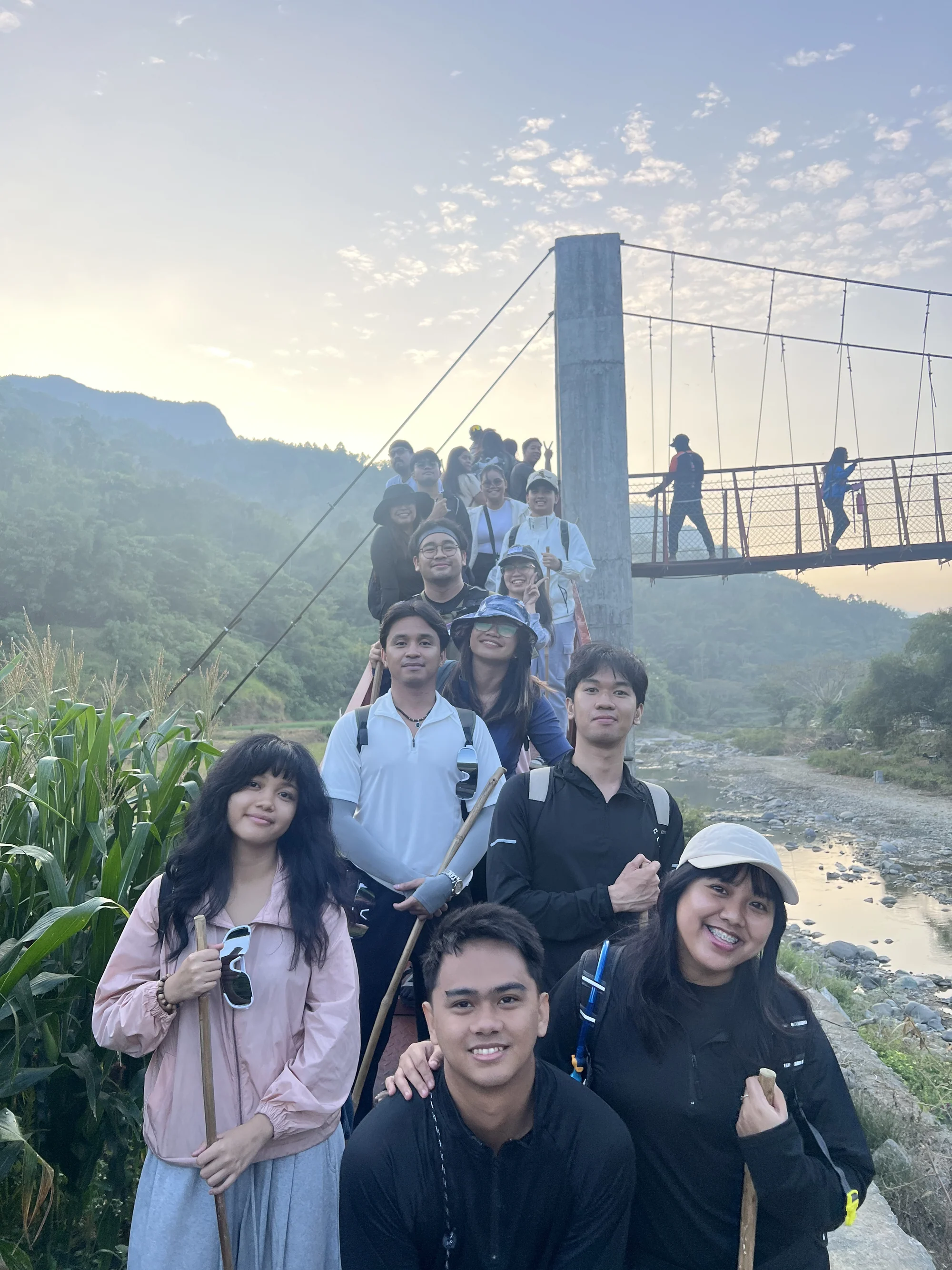 A group photo beside a suspension bridge in the mountains at sunset